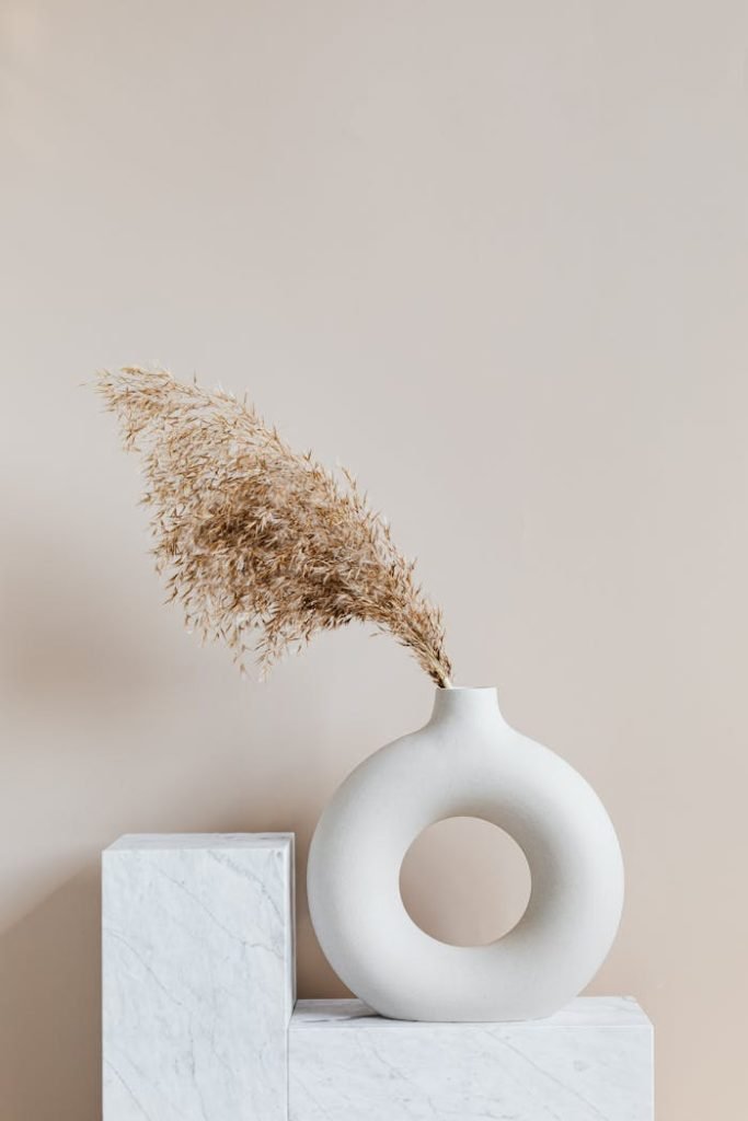 Elegant ceramic vase with dried grass on a marble pedestal, showcasing simplicity and minimalism.
